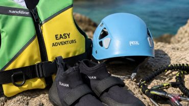 Material técnico de coasteering en Ibiza con casco, chaleco de flotación y escarpines sobre rocas junto al mar
