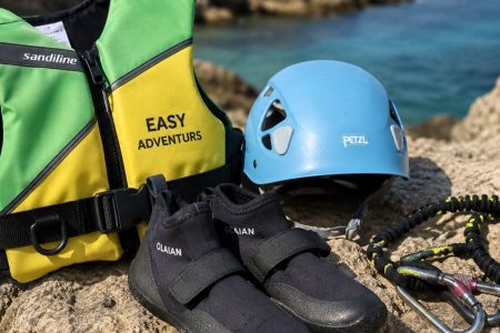 Material técnico de coasteering en Ibiza con casco, chaleco de flotación y escarpines sobre rocas junto al mar