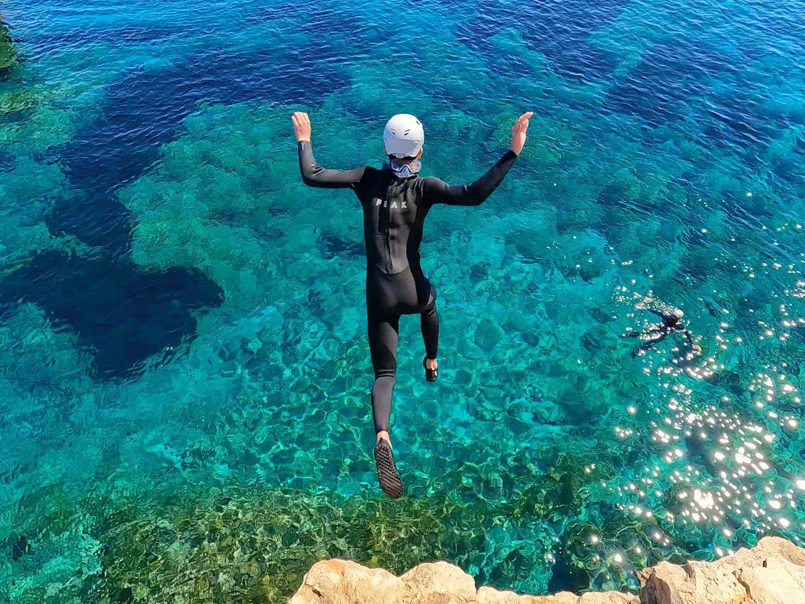 Salto de coasteering con neopreno, casco y escarpines en Ibiza